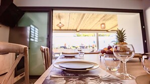 Una mesa de comedor dispuesta con platos, cubiertos y vasos, con una piña y un cuenco de frutas sobre la mesa.