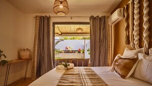 Habitación de hotel con una cama grande, techo de madera, lámpara colgante, ventana con cortinas y vistas a un jardín.