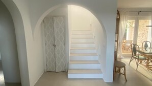 A spacious interior with a staircase leading to a balcony, a patterned door, and a dining area with chairs.