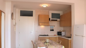 A compact kitchen with wooden cabinets, a gas stove, a microwave, and a refrigerator. - Beach front apartment with sea view (Bibione)