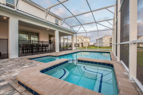Une piscine entourée de parois en verre, un patio aménagé avec du mobilier d’extérieur et une vue sur les maisons voisines.