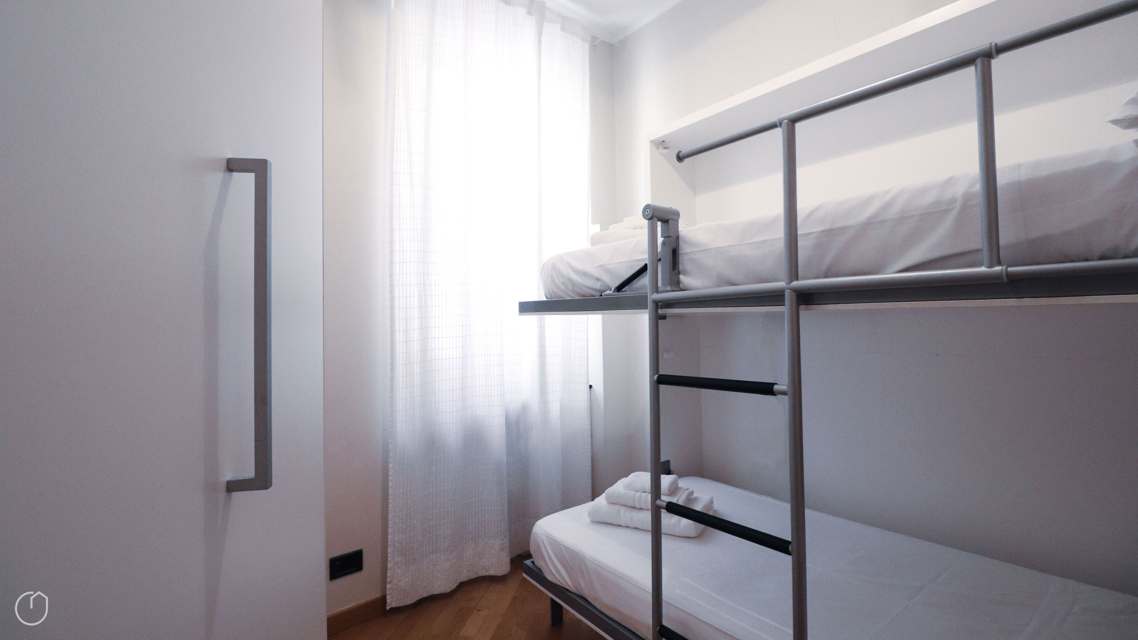 A bunk bed room with a window, a mirror, and a white curtain.