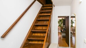 A wooden staircase with a white wall and a door leading to a room with a plant and a chair. - Apartment Bor (Dubrovnik)