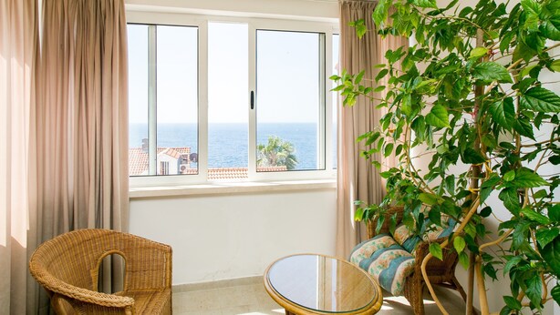A room with a large window, a wicker chair, a small round table, and a sofa. - Apartment Bor (Dubrovnik)