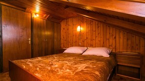 A bedroom with a wooden ceiling, a bed with a patterned bedspread, two bedside tables, and a nightstand. - Apartment Bor (Dubrovnik)
