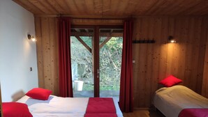 Habitación de cabaña de madera con dos camas, almohadas rojas, techo de madera y vista a un jardín a través de un ventanal.