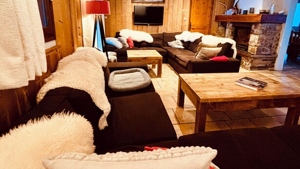 Una sala de estar acogedora con paredes y techo de madera, un televisor de pantalla plana montado en la pared, una chimenea y asientos cómodos.