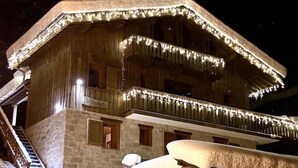 Una cabaña de madera con fachada de piedra, varios balcones e iluminación festiva.