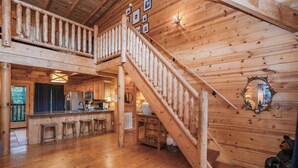 LâintĂ©rieur dâune cabane en bois comprend un escalier central, un coin cuisine et un bar avec des tabourets.