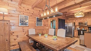 Une cuisine aux murs lambrés, avec une table à manger en bois, des chaises, un banc et un luminaire suspendu.