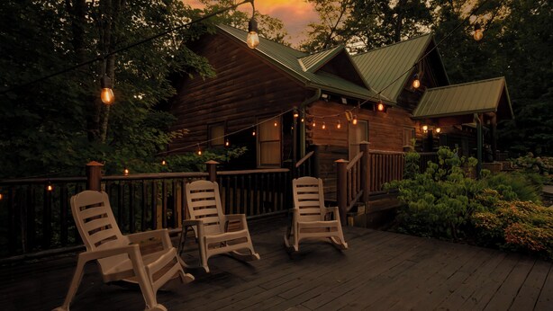 Une cabane en bois avec une véranda, des fauteuils à bascule et des guirlandes lumineuses.