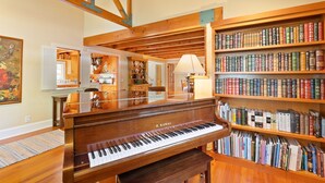 Um piano de cauda, estantes de livros e uma sala de jantar com vigas de madeira e um quadro.