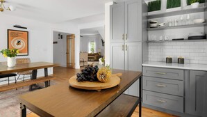 Una cuina moderna amb armaris grisos, una taula de dinar de fusta i un plat de fruita.