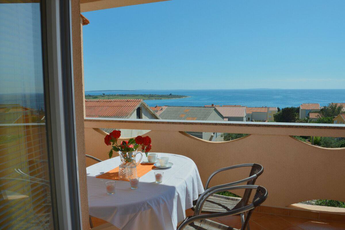 A balcony with a table set for two, overlooking a coastal view.
