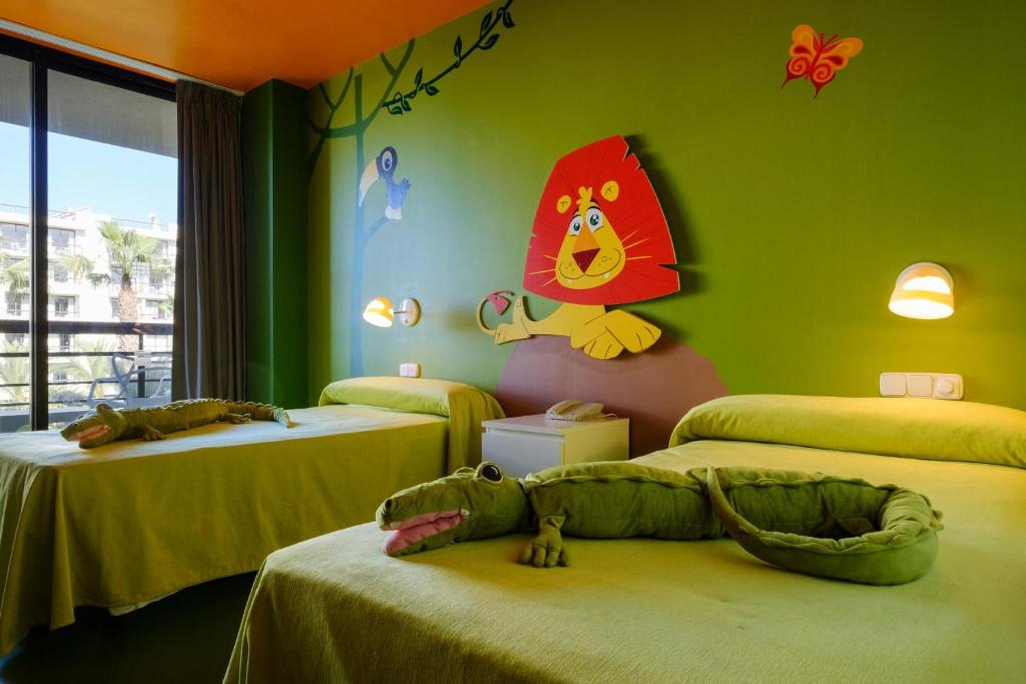 A hotel room with two beds, a large wall mural, and a window with a view of palm trees.