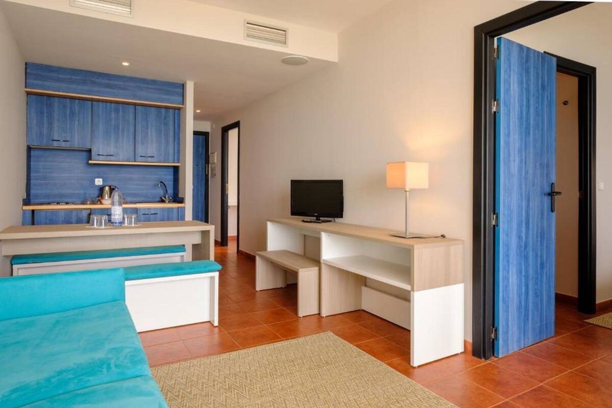 Ein modernes Hotelzimmer mit Küchenzeile, Flachbildfernseher, Sofa und einer Tür zu einem weiteren Raum.