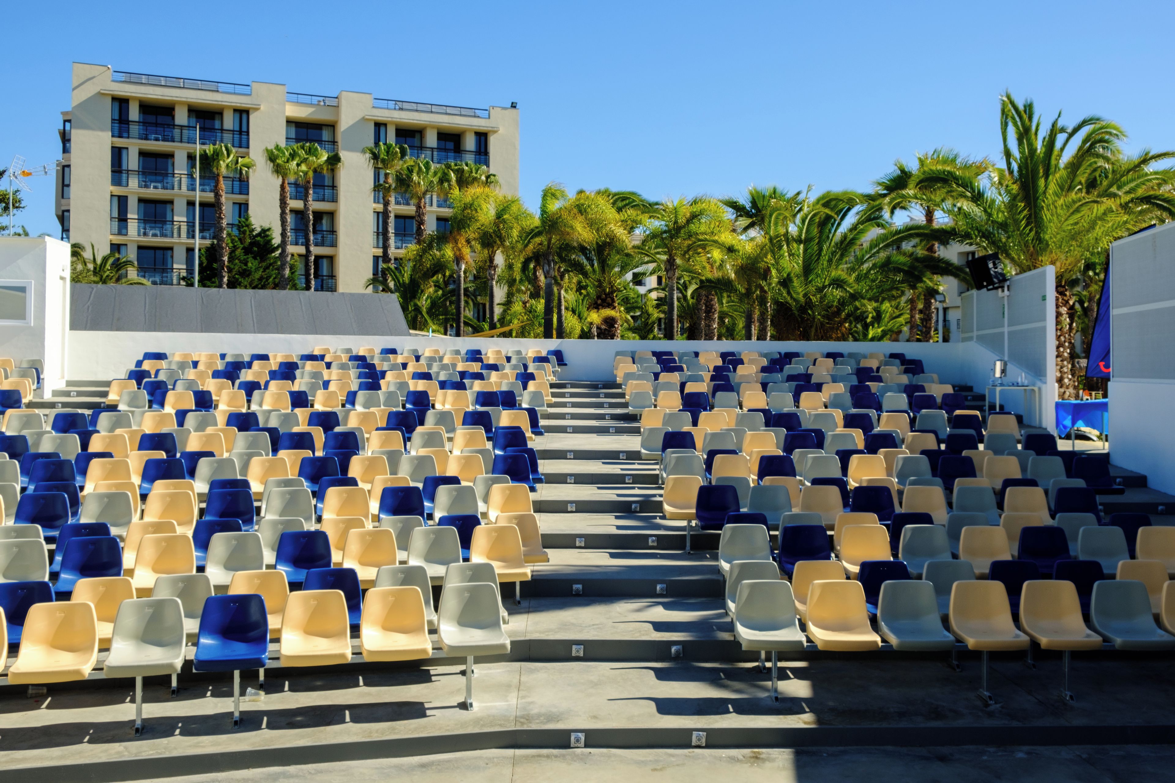 A seating area with rows of chairs, a building in the background, and palm trees.