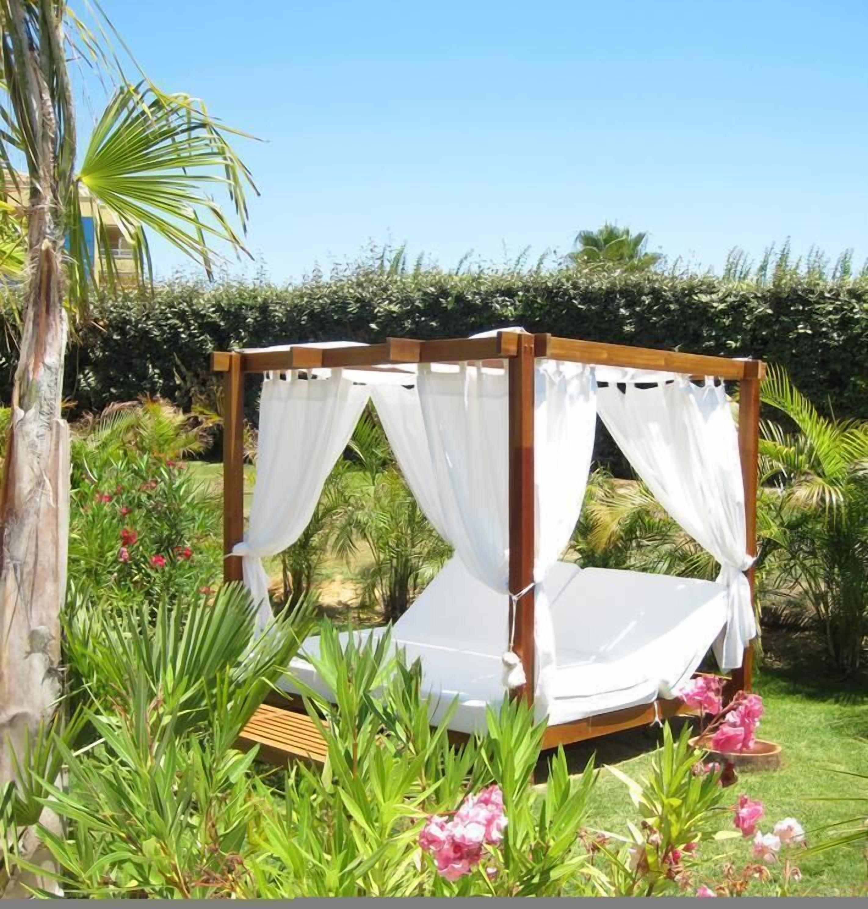 Una cama con dosel de madera y cortinas blancas en un exuberante jardín.