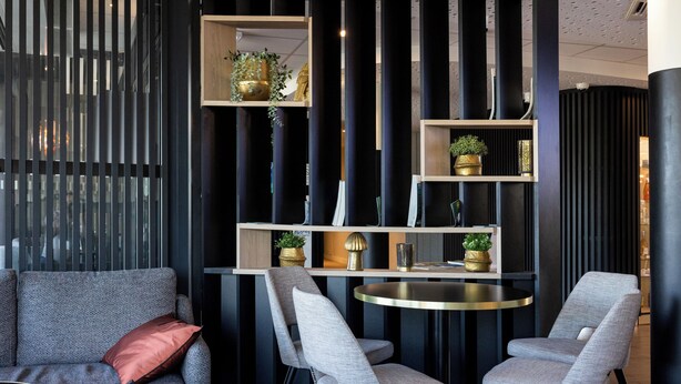 A modern interior with a sofa, two chairs, a round table, and a decorative shelf with plants. - Hôtel AKENA TROYES - La Chapelle-Saint-Luc (La Chapelle-Saint-Luc)
