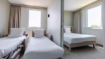 A hotel room with two single beds, a large window, and a sliding door leading to a bathroom.