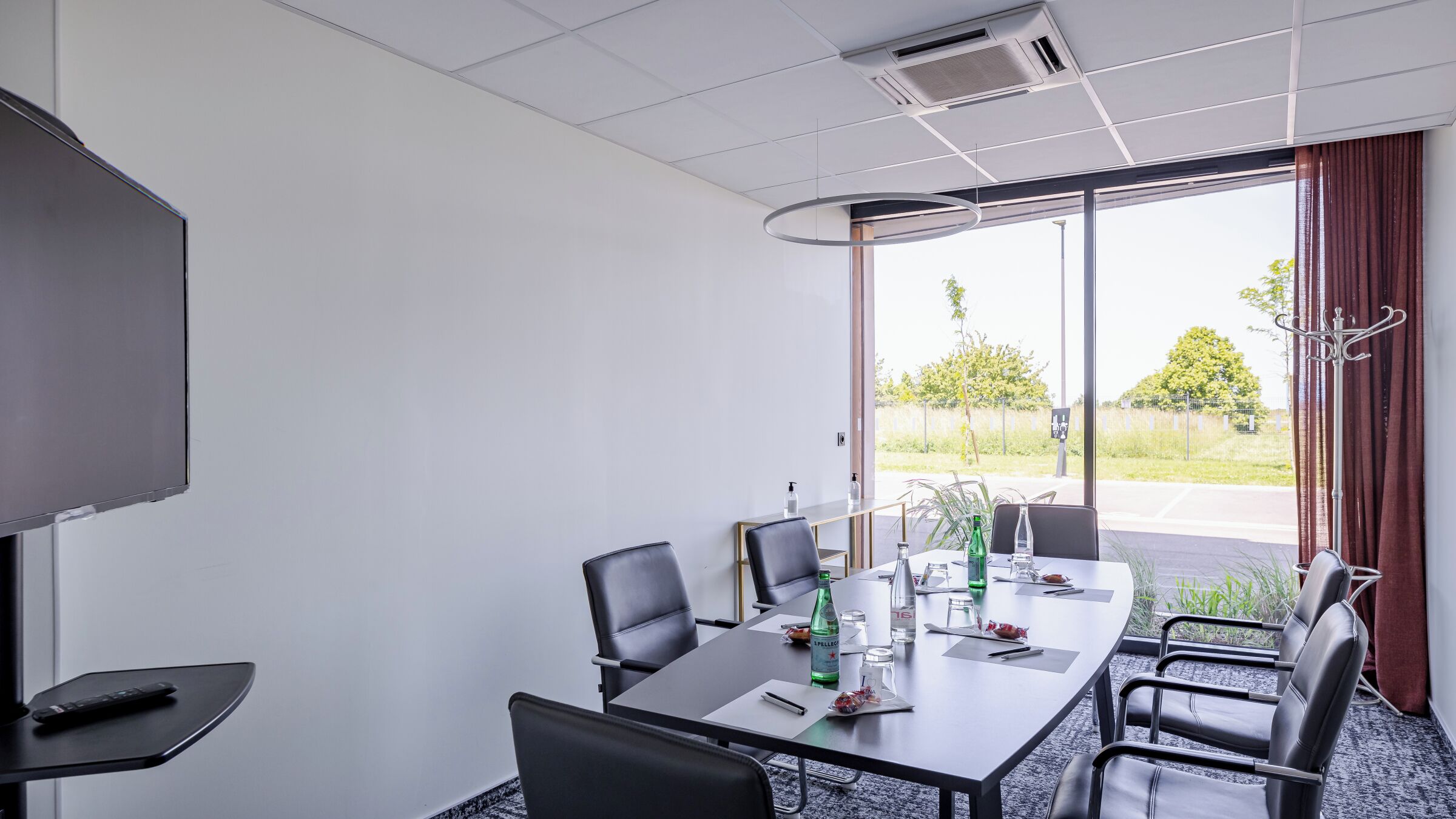 A conference room with a large table, chairs, a projector screen, and a view through the glass door.