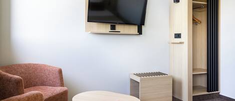 A room with a mounted TV, a wooden wardrobe, a small table, and two chairs.