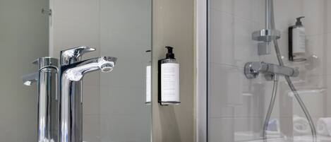 Un baño con grifo cromado, lavamanos blanco y cabina de ducha con paredes de vidrio.