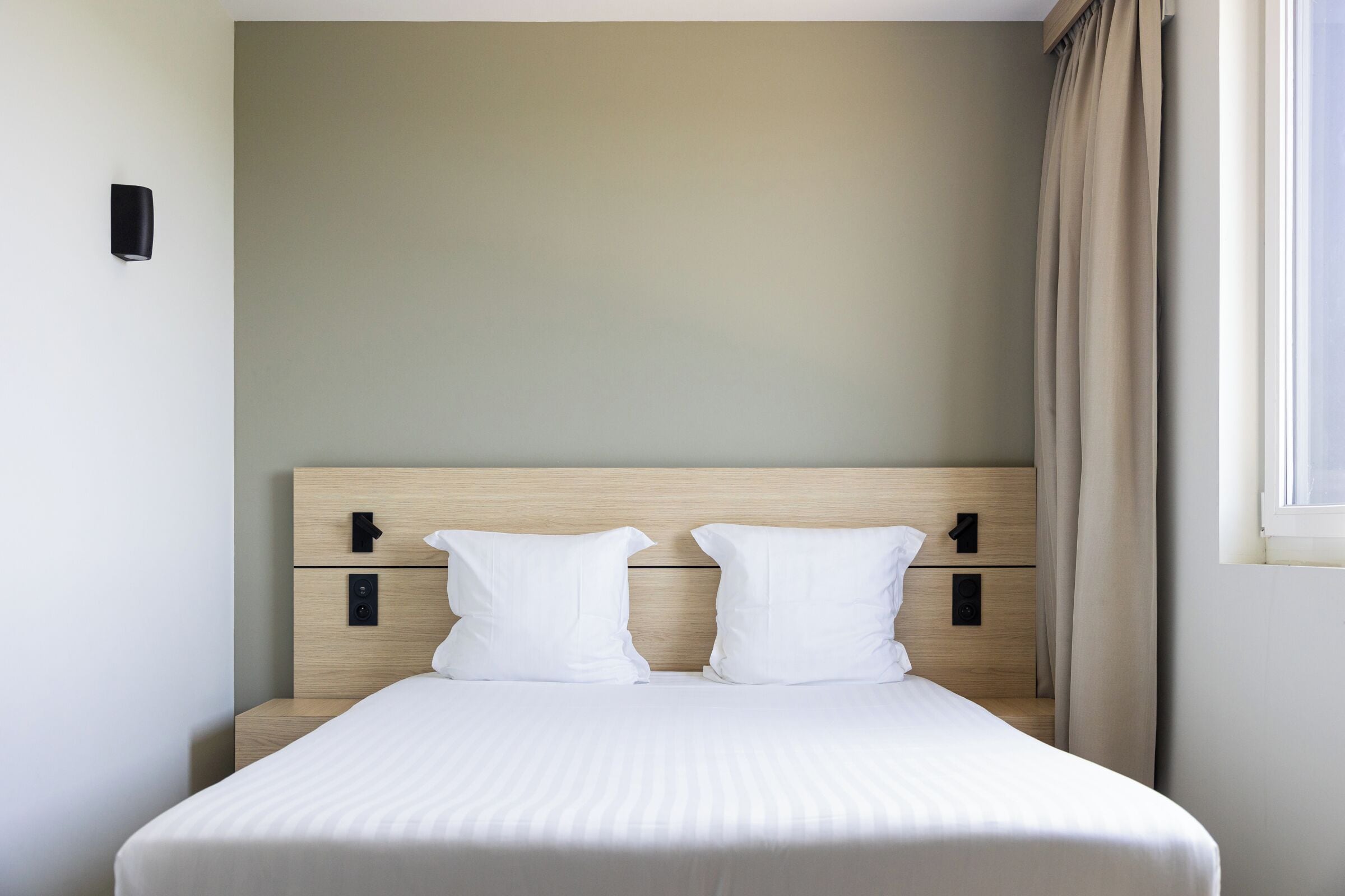 A neatly made bed with a wooden headboard, two pillows, and a bedside table with a lamp.