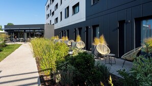 A modern building with outdoor seating and greenery. - Hôtel AKENA TROYES - La Chapelle-Saint-Luc (La Chapelle-Saint-Luc)