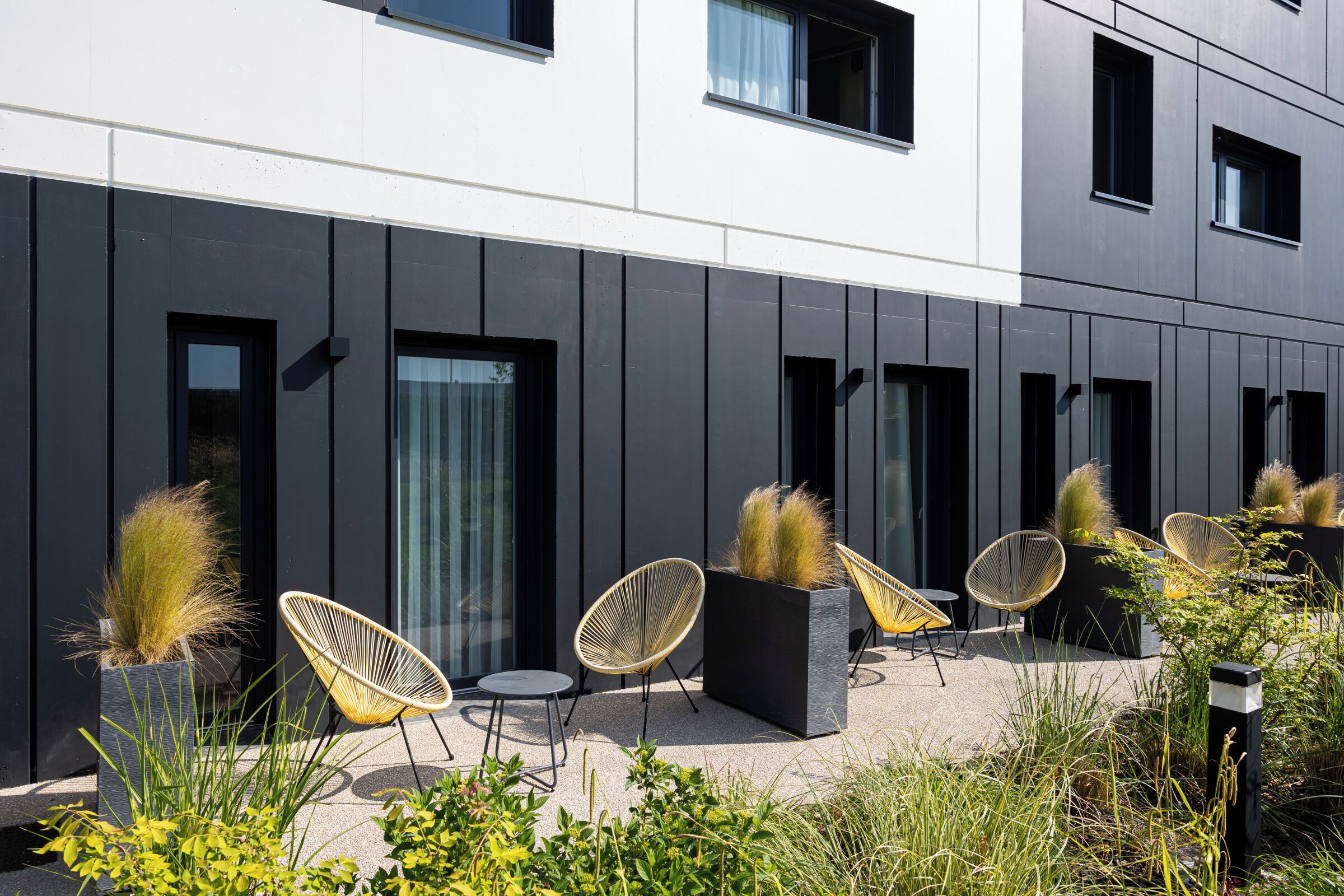 A modern building with a flat facade, large windows, and outdoor seating with chairs and planters.