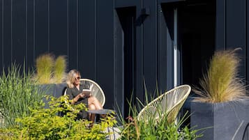 Une personne est assise dans un fauteuil en osier à l’extérieur d’un bâtiment à la façade sombre et lit un livre.