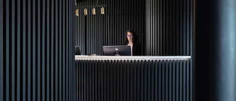 En receptionsdisk med en bärbar dator, en svartvitmönstrad vägg och ett tak med en lampa.
