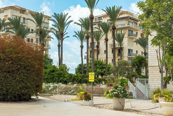 A multi-story residential building with balconies, surrounded by palm trees and potted plants.