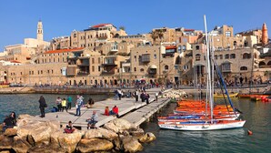 A coastal town with historic buildings, a dock with colorful boats, and a clear blue sky. - MAMAD - Deluxe 2BD Jaffa Dreams W Pool & Parking (Tel Aviv)