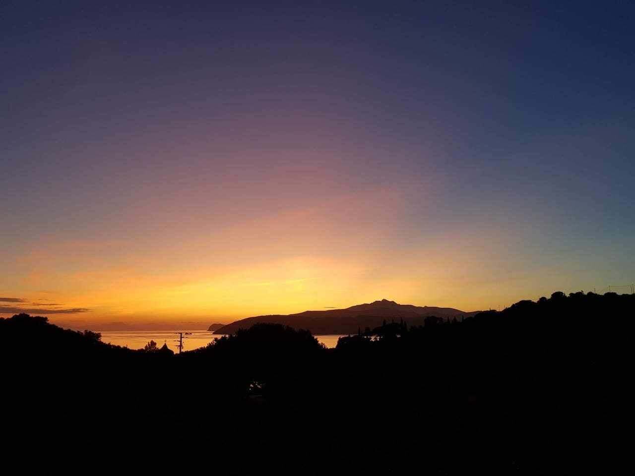 A sunset view with silhouettes of hills and a body of water.