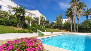 Una piscina con un edificio blanco al fondo, rodeada de follaje y palmeras.