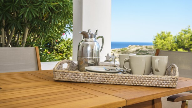 Una mesa de madera con una bandeja que sostiene una jarra de plata, dos tazas blancas y un plato con una cuchara.