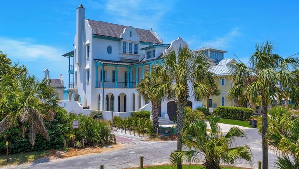 A large, white, multi-story building with a prominent balcony and arched windows, surrounded by lush greenery and palm trees. - Intensive Care ~ Steps From the Ocean w/ Golf Cart + Free Attraction Tickets! (Santa Rosa Beach)