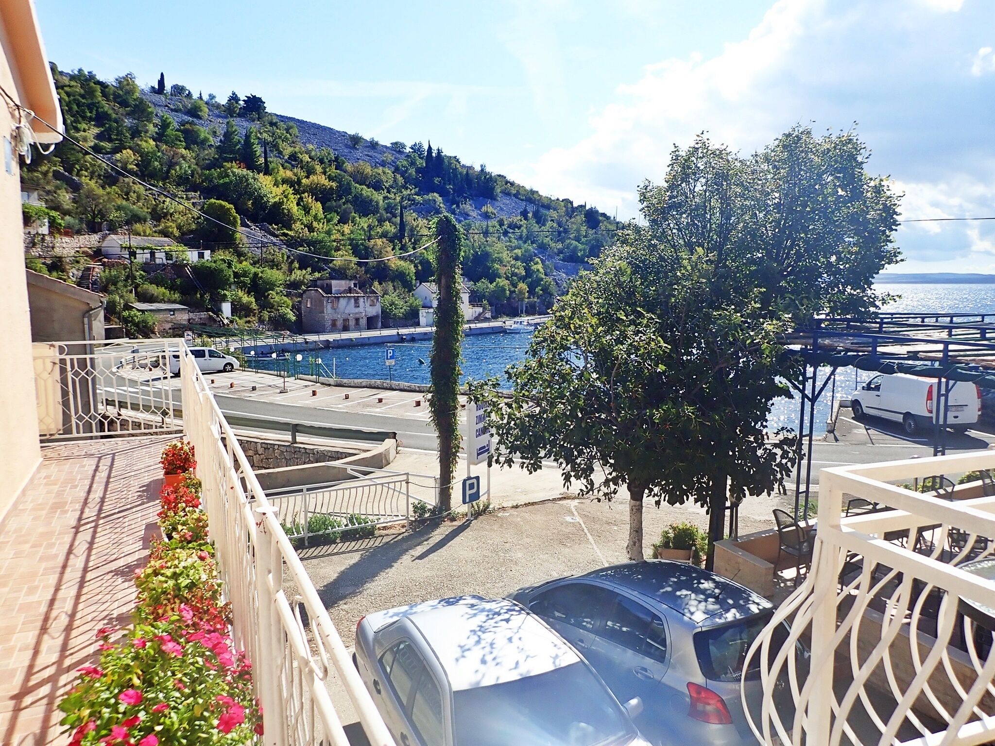 A balcony with a view of a coastal area, a parking lot, and a building with a sign.
