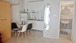 Eine kompakte Küche mit weißen Schränken, ein Essbereich mit kleinem Tisch und Stühlen sowie ein Badezimmer mit Waschbecken und Spiegel.