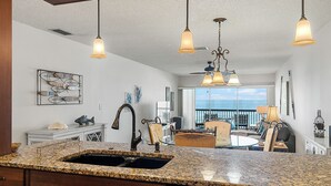 A kitchen with granite countertops, a dishwasher, and a dining area with a view. - Seaside Beach House 203 · Top Floor · 14-Ft Balcony · Pool (Holmes Beach)