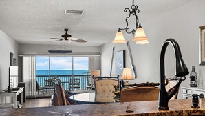 A kitchen with a large island, a ceiling fan, and a view of the ocean. - Seaside Beach House 203 · Top Floor · 14-Ft Balcony · Pool (Holmes Beach)