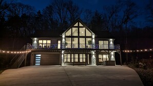 Een modern huis met twee verdiepingen, een ruime garage, een overdekte veranda en een balkon met lichtslingers.