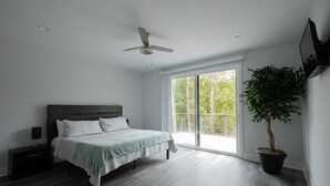 Een slaapkamer met een bed, nachtkastje, plafondventilator, groot raam en een kamerplant.