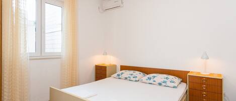A bedroom with a bed, two bedside tables with lamps, a wooden nightstand, and a window with curtains.