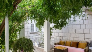 A covered outdoor seating area with a sofa and table, surrounded by greenery and a stone wall. - Guest House Ljubica (Dubrovnik)