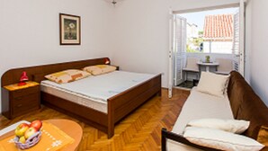 A bedroom with a wooden bed, a nightstand, a table with fruit, a chair, and a door leading to an outdoor area. - Guest House Ljubica (Dubrovnik)