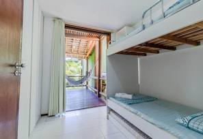 Quarto com beliches, uma rede e vista para um deck de madeira e vegetação lá fora.