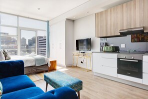 A modern apartment with a large window, a sofa, a small table, a kitchen with a Bosch oven, and a television. - Backup-Power Lavish Eclectic City View Apartment on Popular Bree Street (Cape Town)