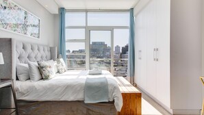 A modern bedroom with a large bed, a view of the city, and a cityscape through the windows. - Backup-Power Lavish Eclectic City View Apartment on Popular Bree Street (Cape Town)